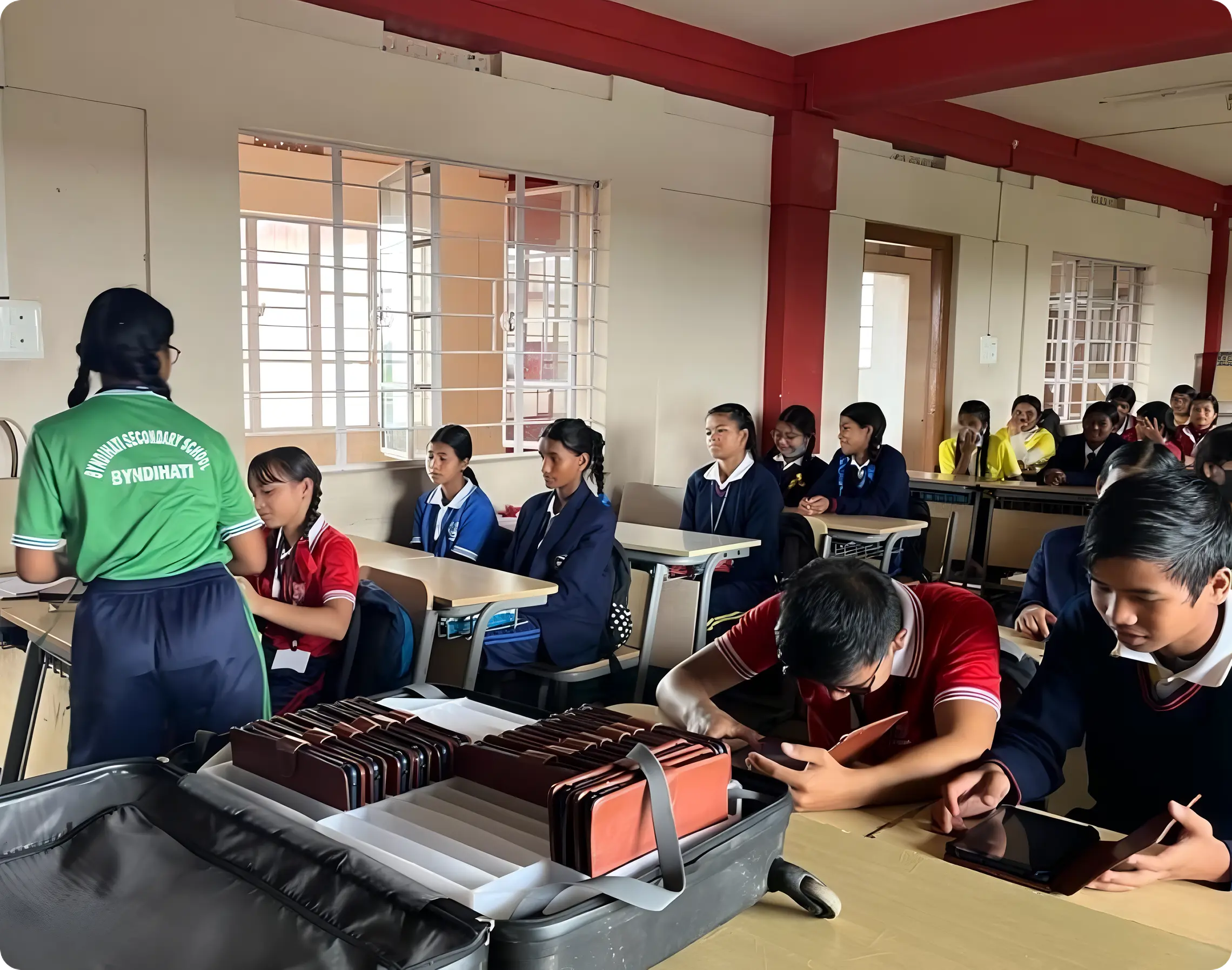Students distributing tablets to peers from a suitcase-based digital library setup for monthly assessments